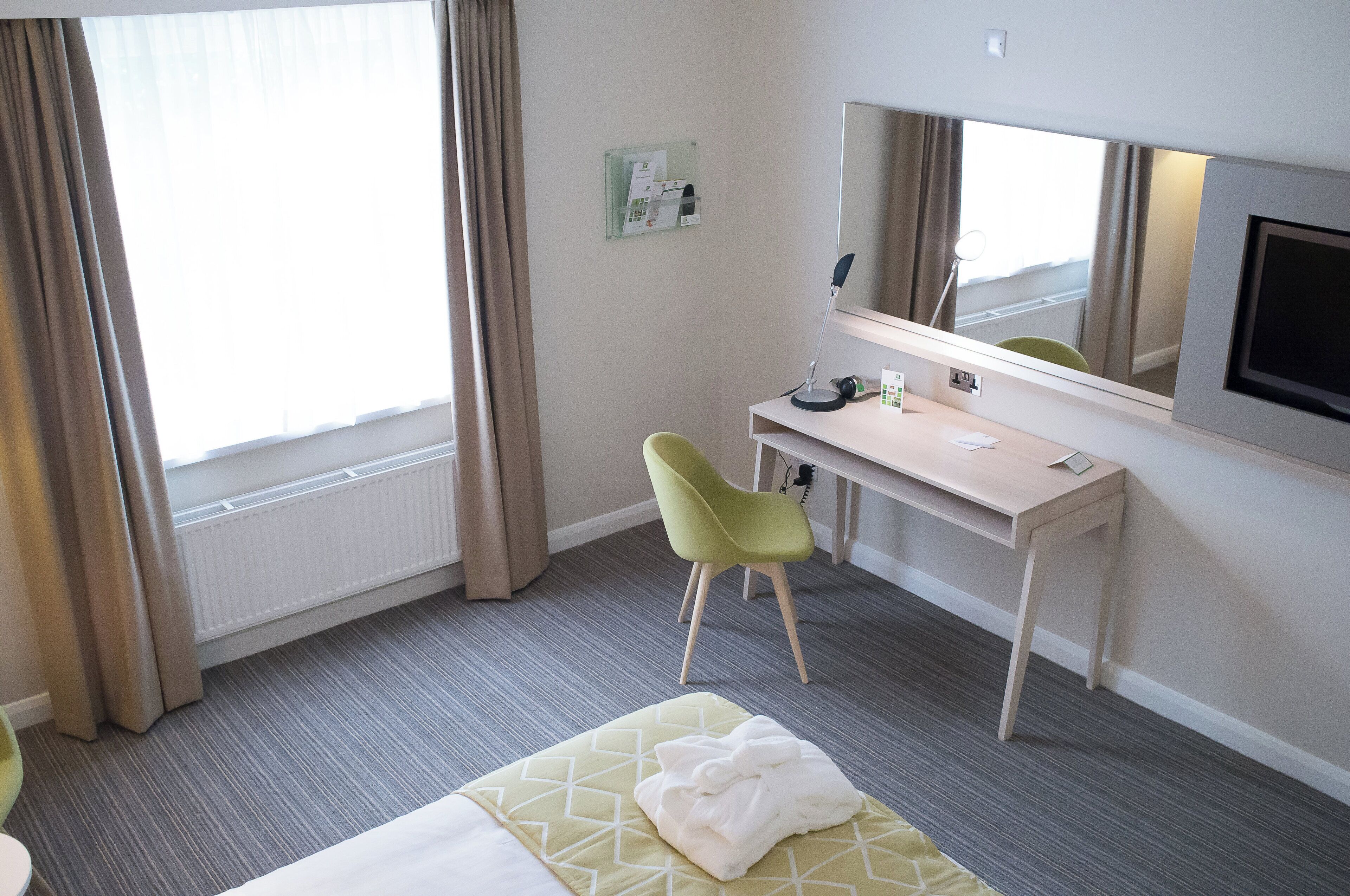 A hotel room with a bed, a desk, a chair, a television, and a window with curtains.
