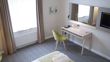 A hotel room with a bed, a desk, a chair, a television, and a window with curtains.