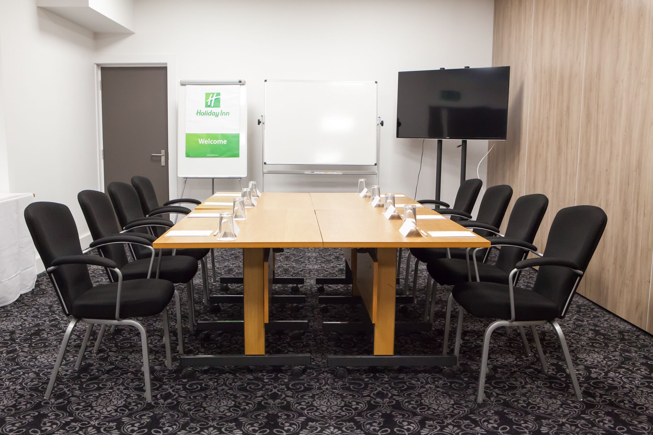 A conference room with a large table, black chairs, a whiteboard, and a television.