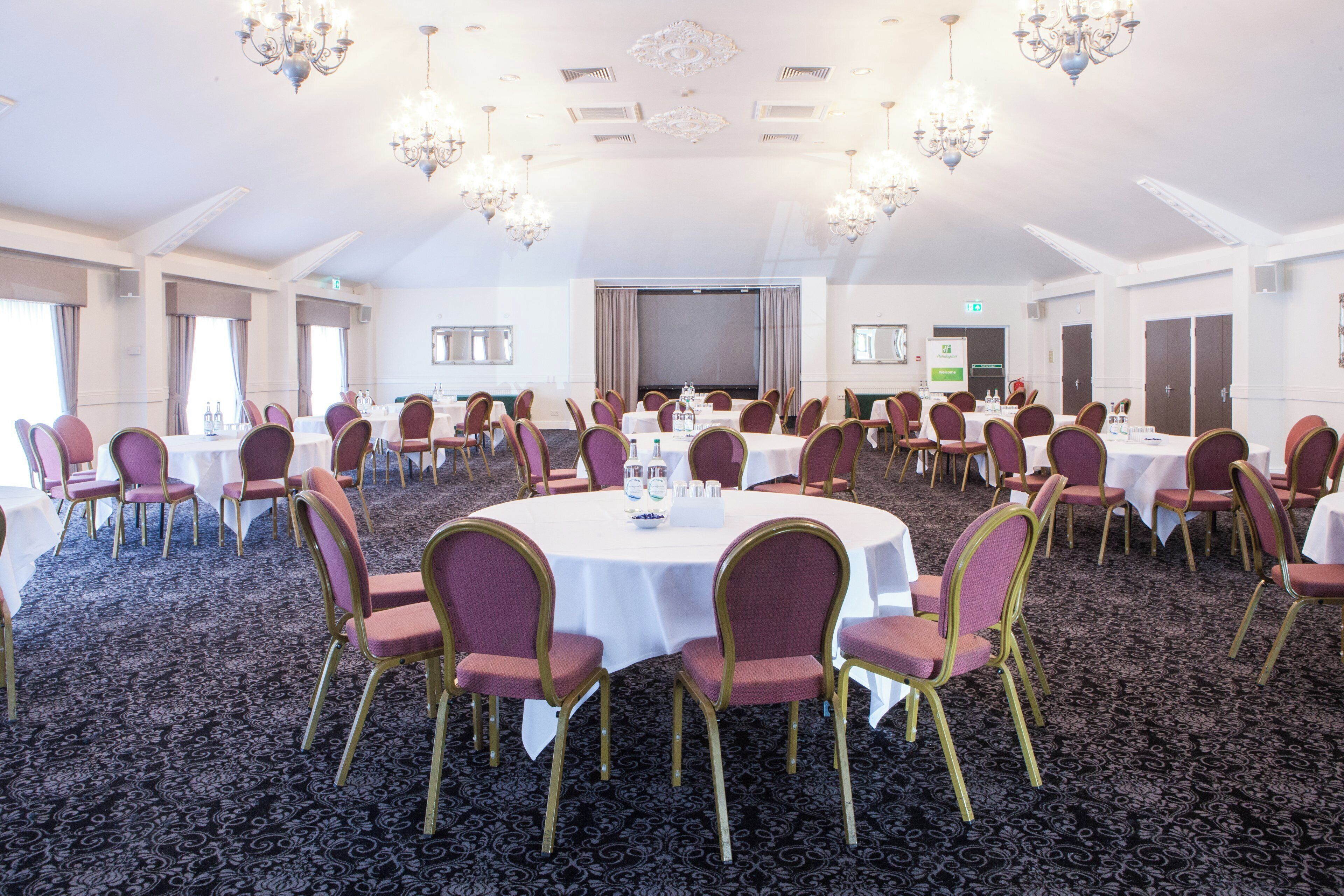 A conference room with round tables, chairs, and chandeliers.