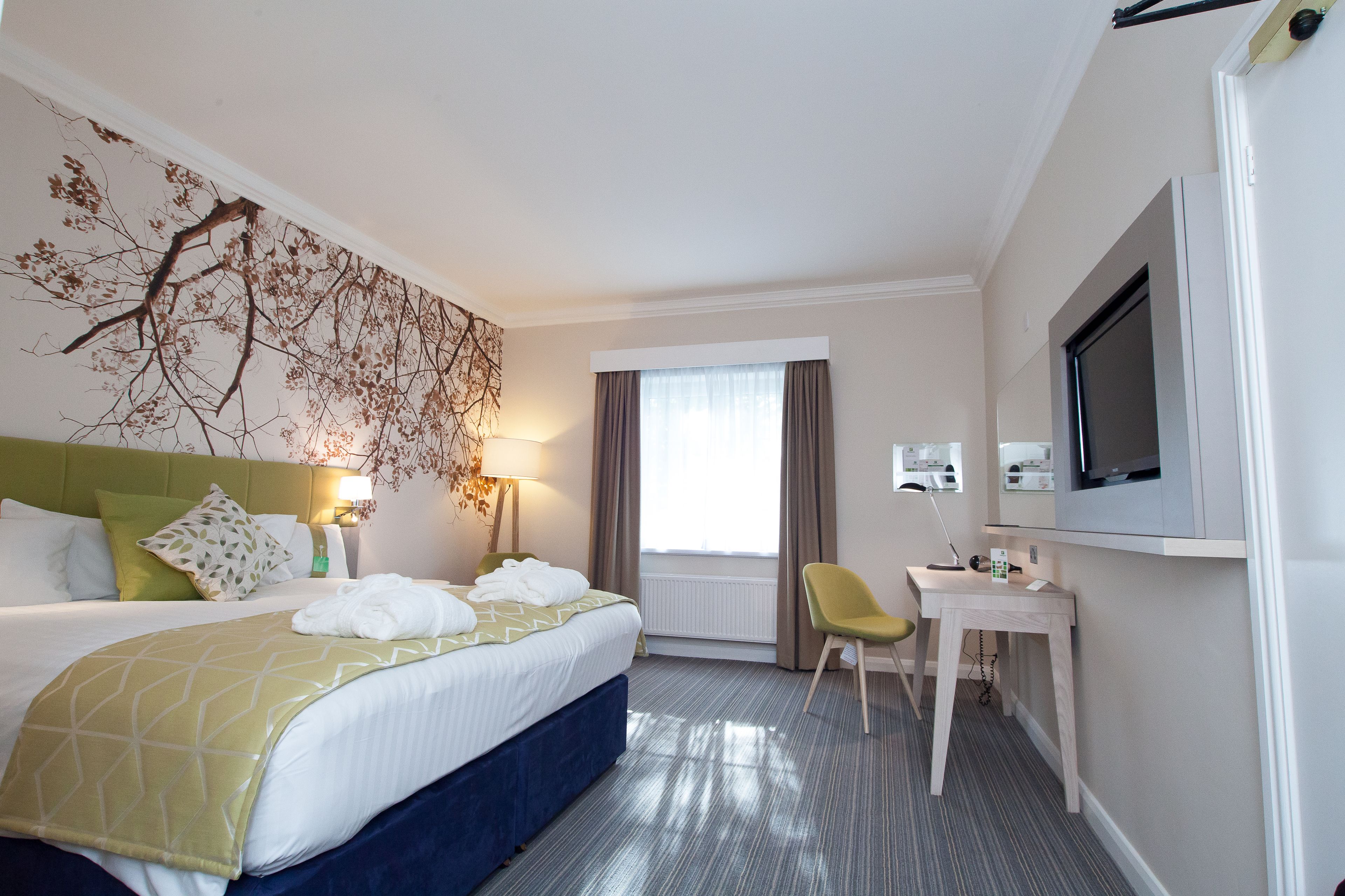 A hotel room with a bed, a desk, a television, and a window with curtains.
