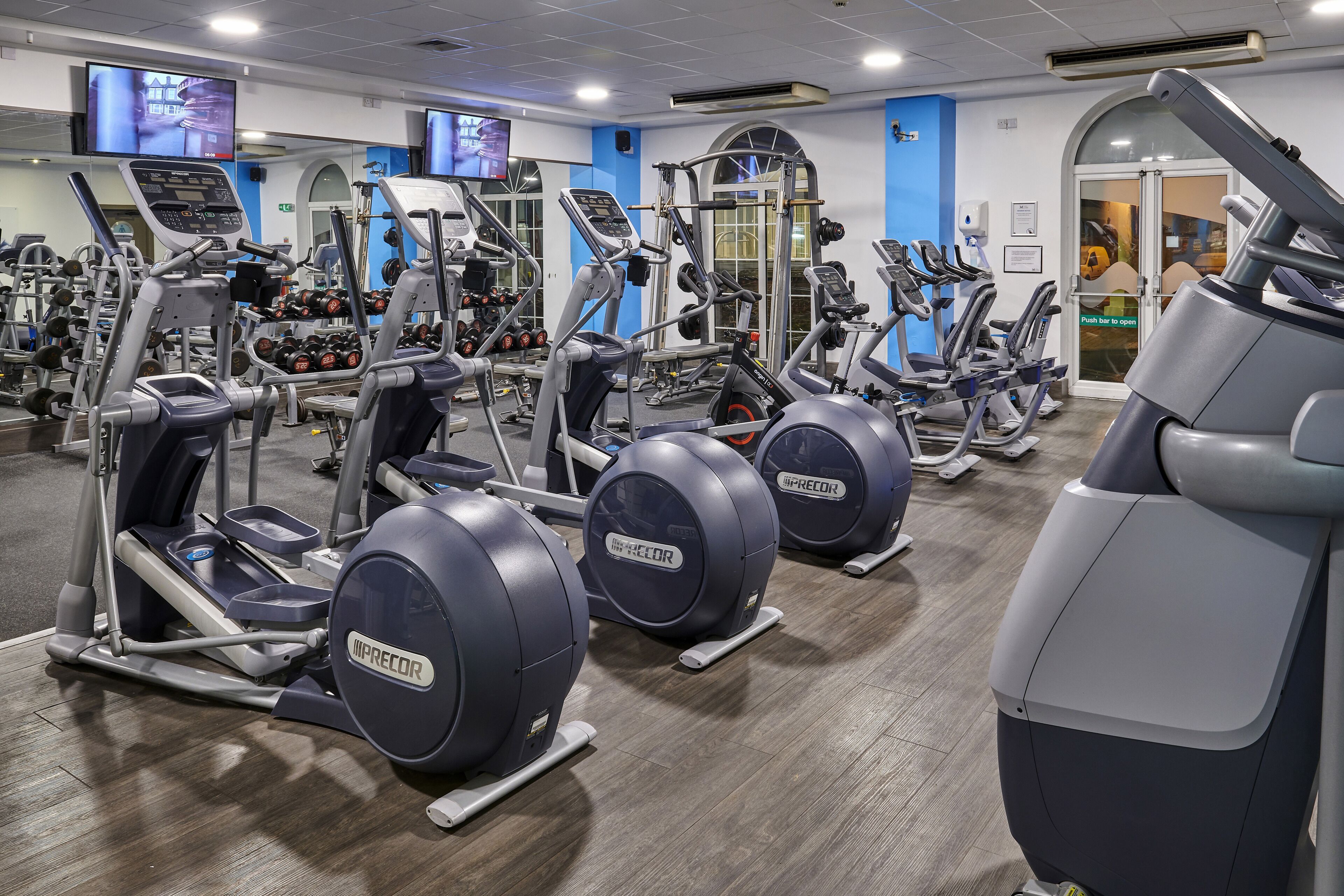 Een sportschool met meerdere fitnessapparaten, waaronder loopbanden en elliptische trainers, gerangschikt in rijen.