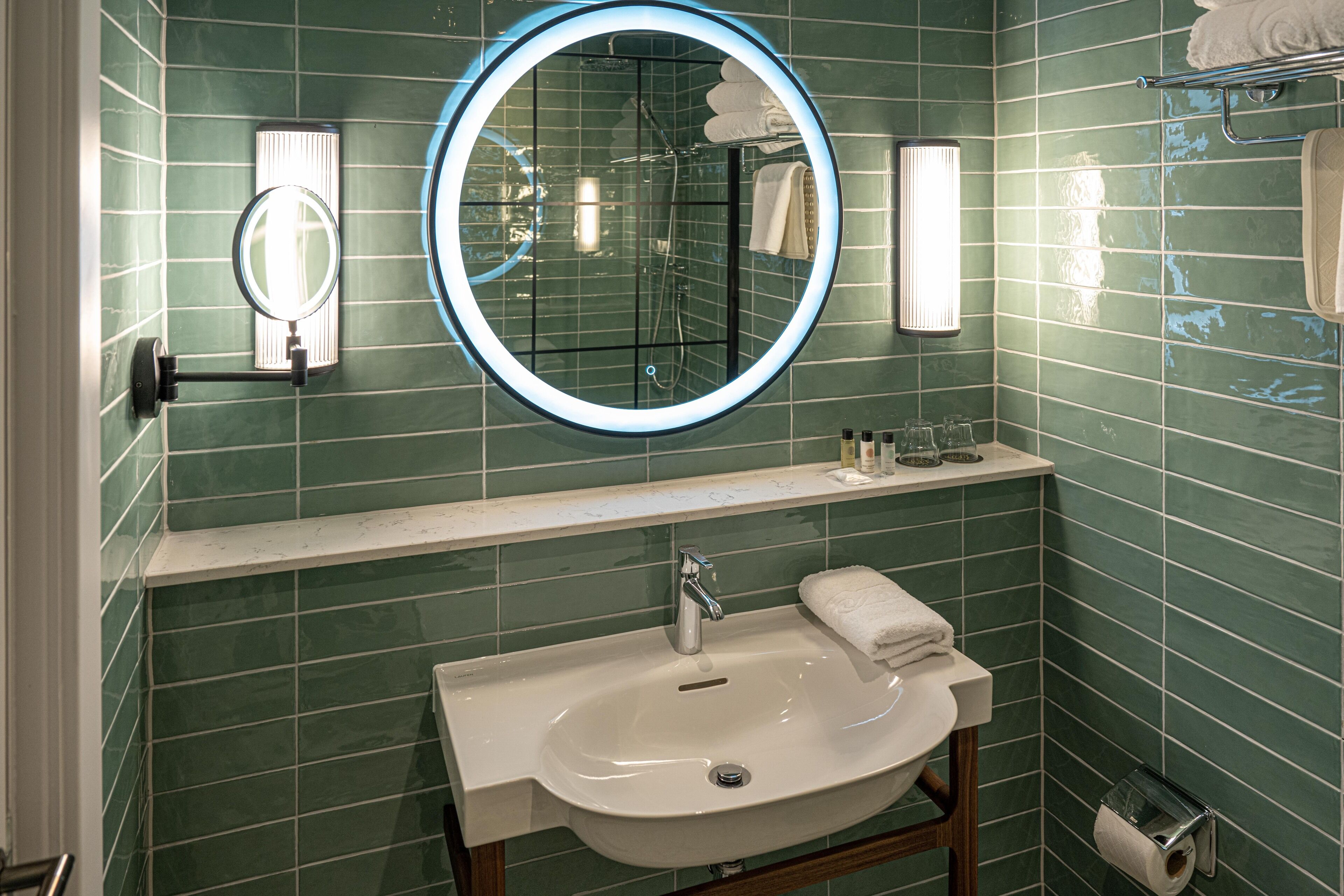 Un baño con un espejo redondo, un lavabo y un perchero para toallas.