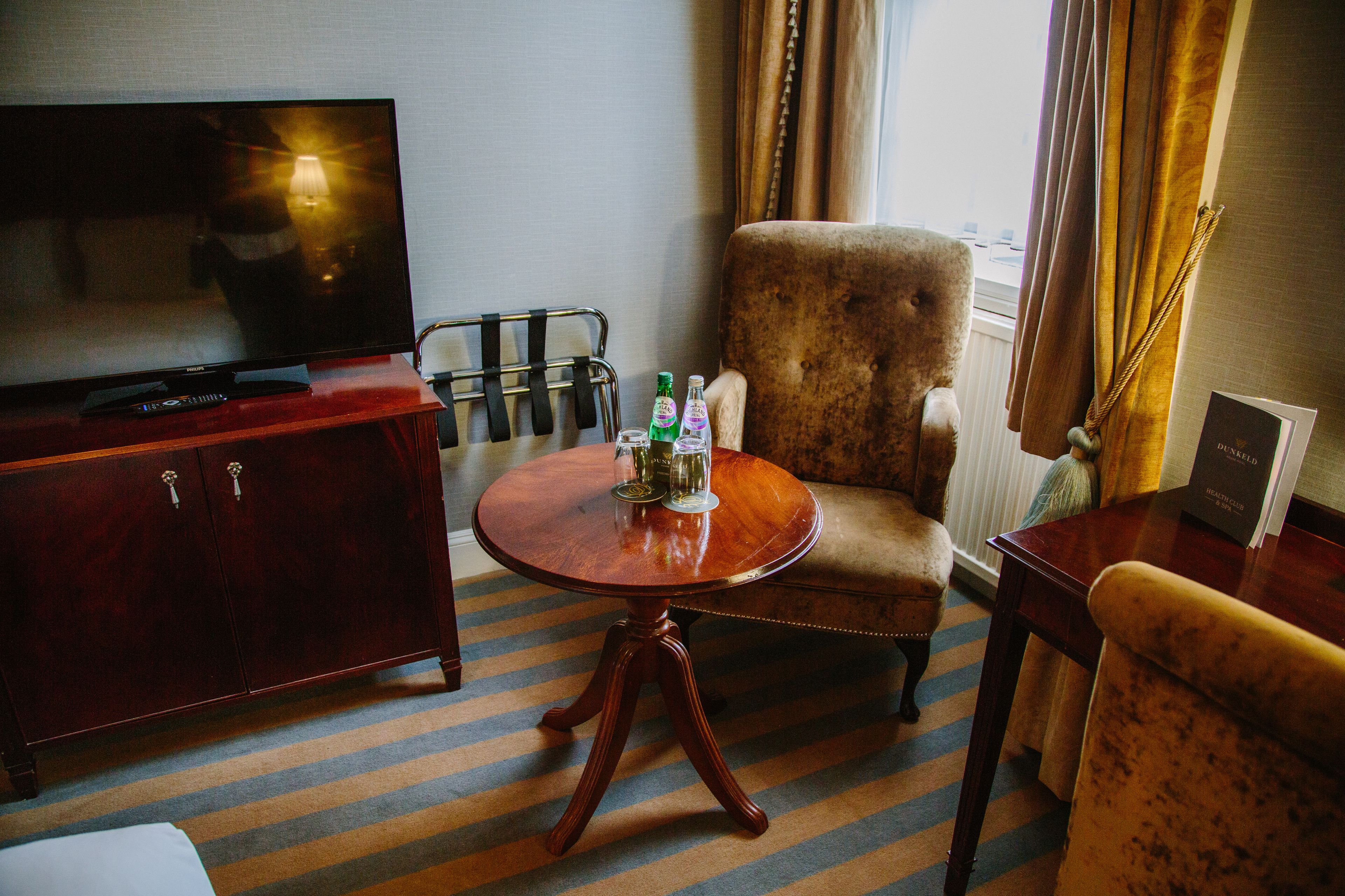 Een hotelkamer met een televisie, een ronde houten tafel met flessen, een bank en een stoel.