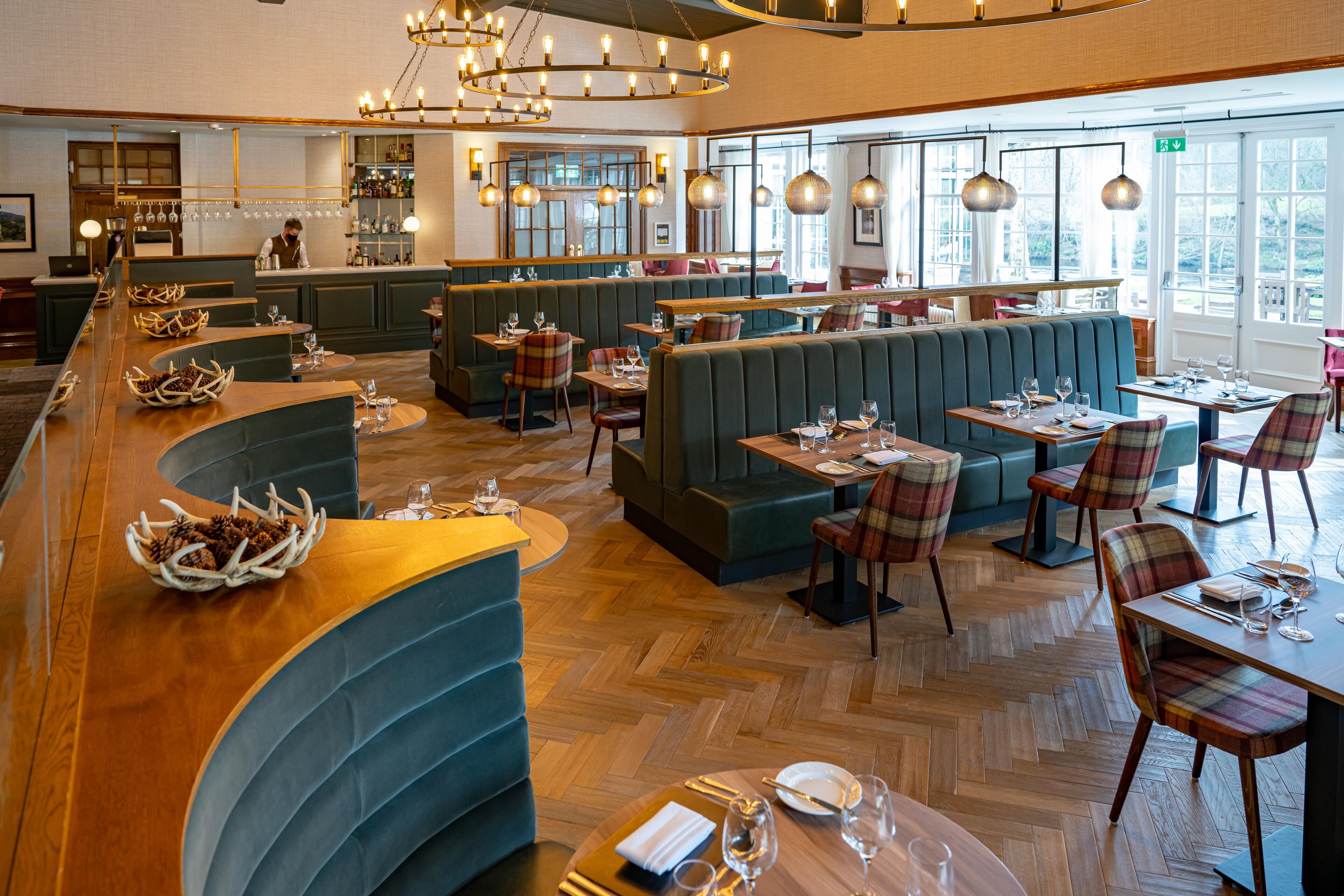 Un restaurante con barra de madera, asientos tipo cabina verdes y sillas a cuadros.