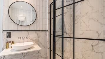 Une salle de bain moderne avec un grand lavabo ovale, un miroir rond et une douche séparée par des parois en verre.