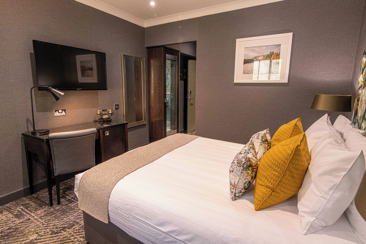 A hotel room with a large bed, a desk, a television, and a door leading to a bathroom.