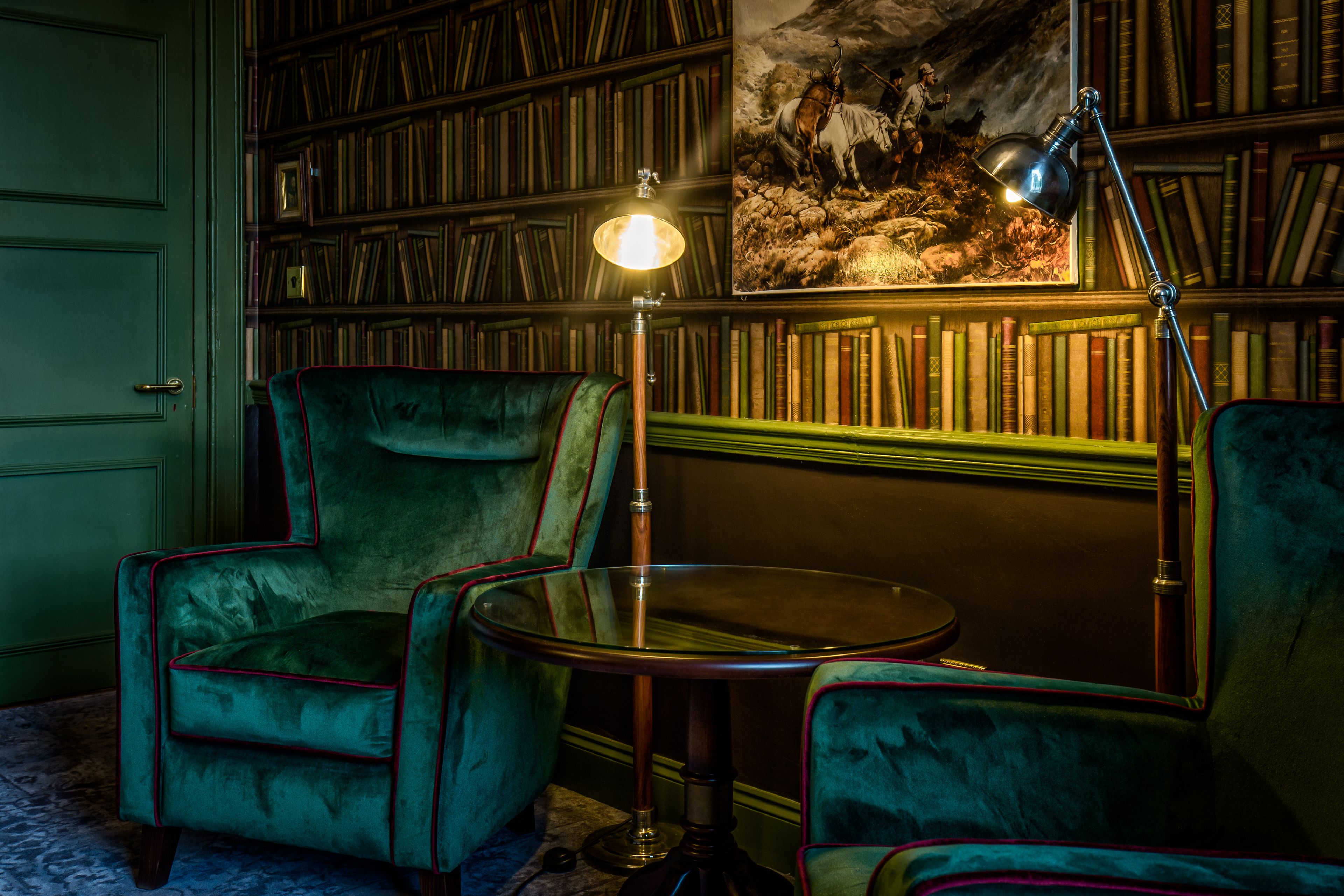 A room with a green armchair, a round table, and a bookshelf filled with books.