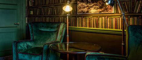 A room with a green armchair, a round table, and a bookshelf filled with books.