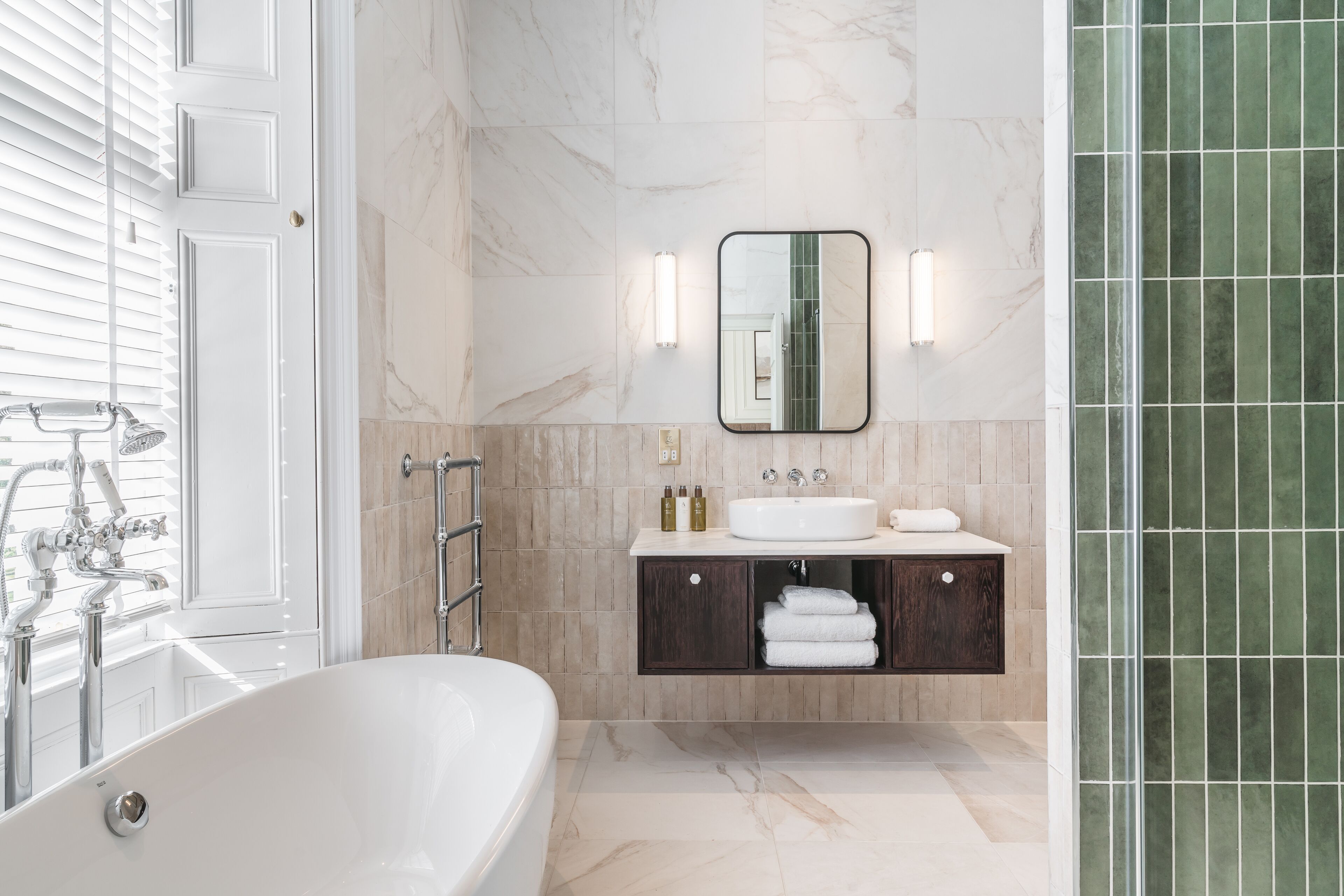 Ein modernes Badezimmer mit freistehender Badewanne, einem Waschtisch mit Spiegel und einer duschgeflieselten Duschzone.