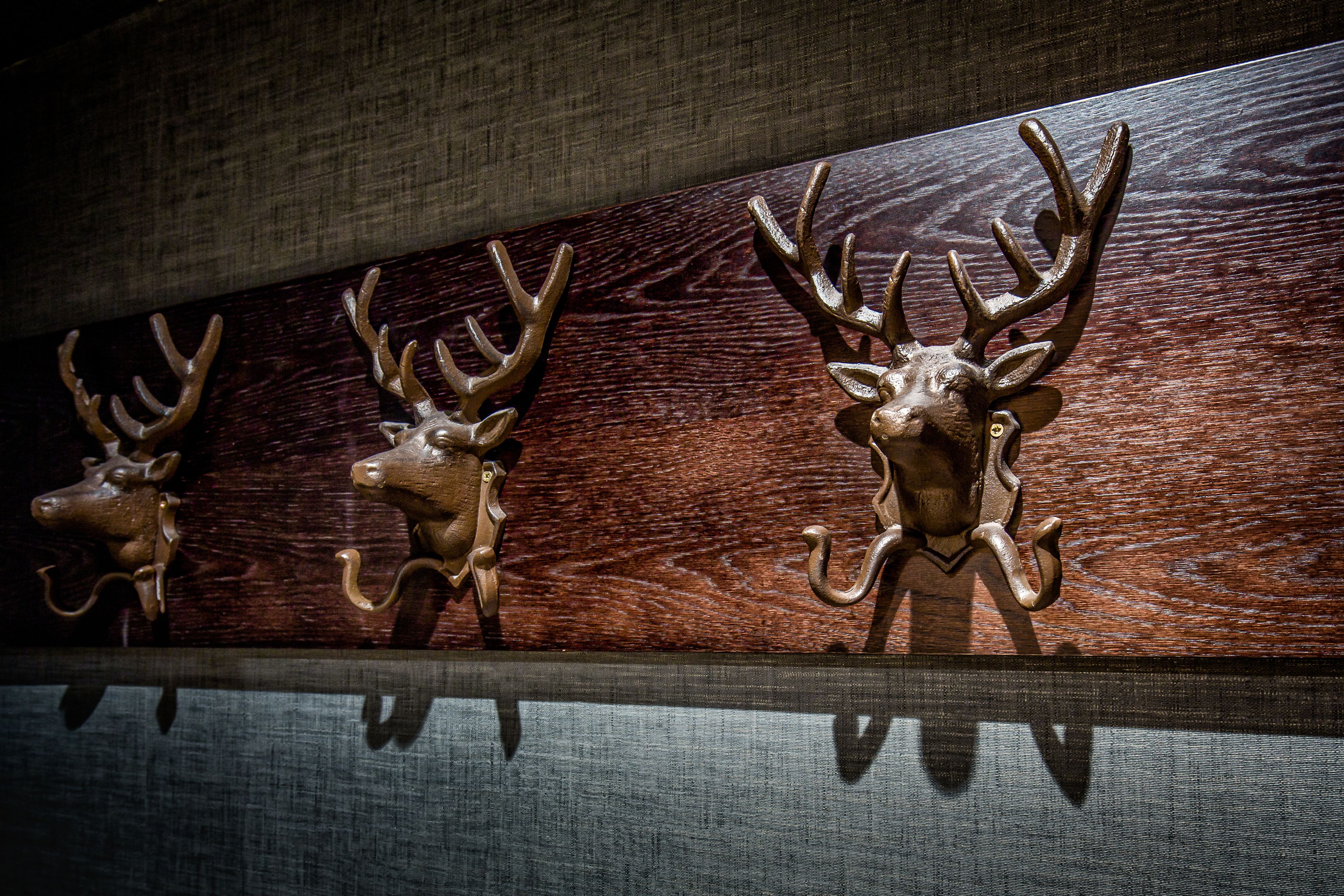 Een houten wand met drie metalen haakjes in de vorm van hertenkoppen.