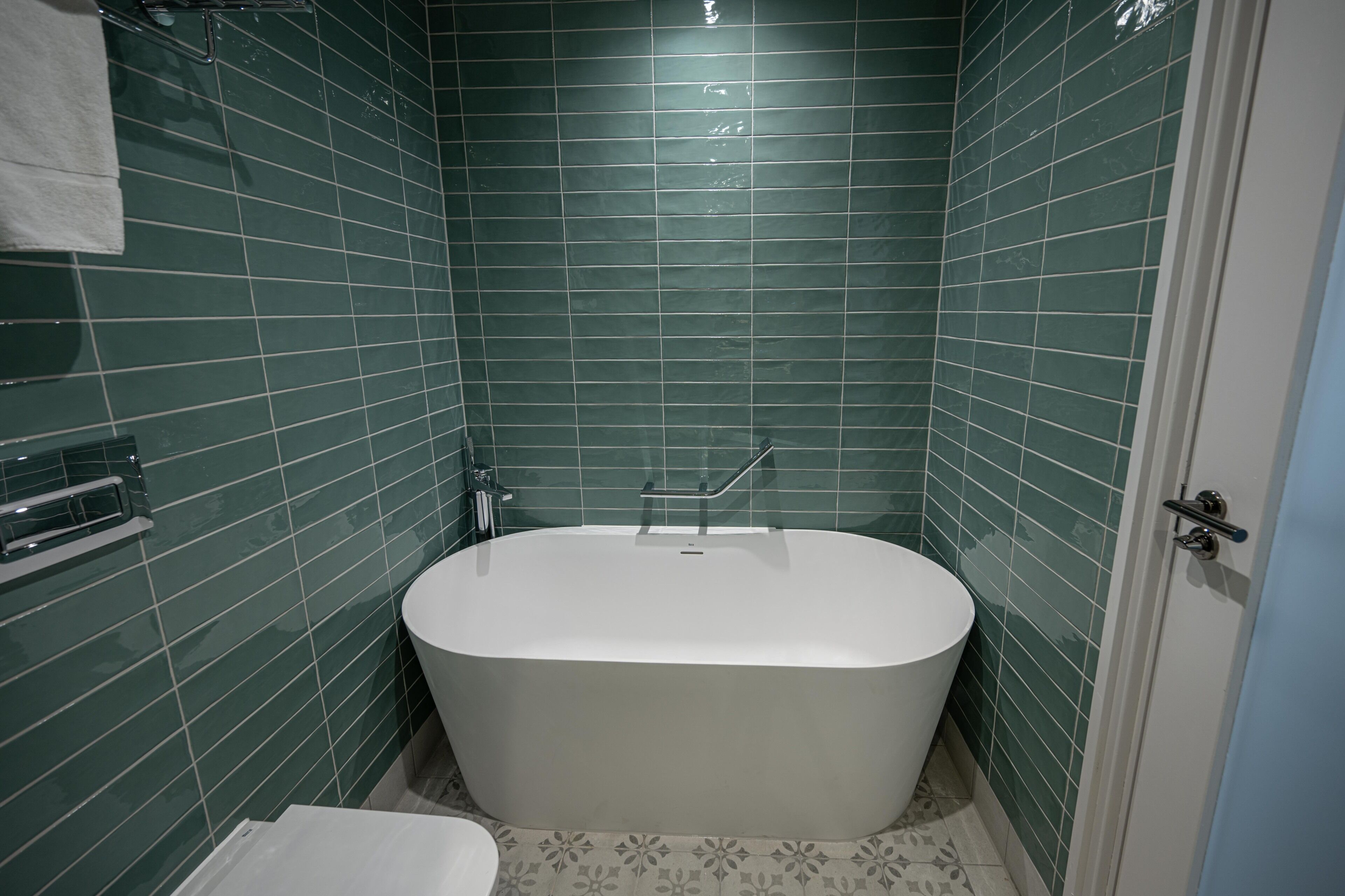 A bathroom with a white bathtub, green tiled walls, a white toilet, and a towel rack.