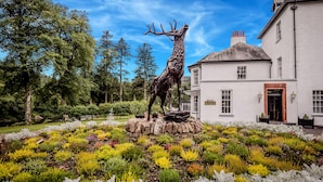 A deer statue on a pedestal in a garden with a white building in the background. - Dunkeld House Hotel (Dunkeld)