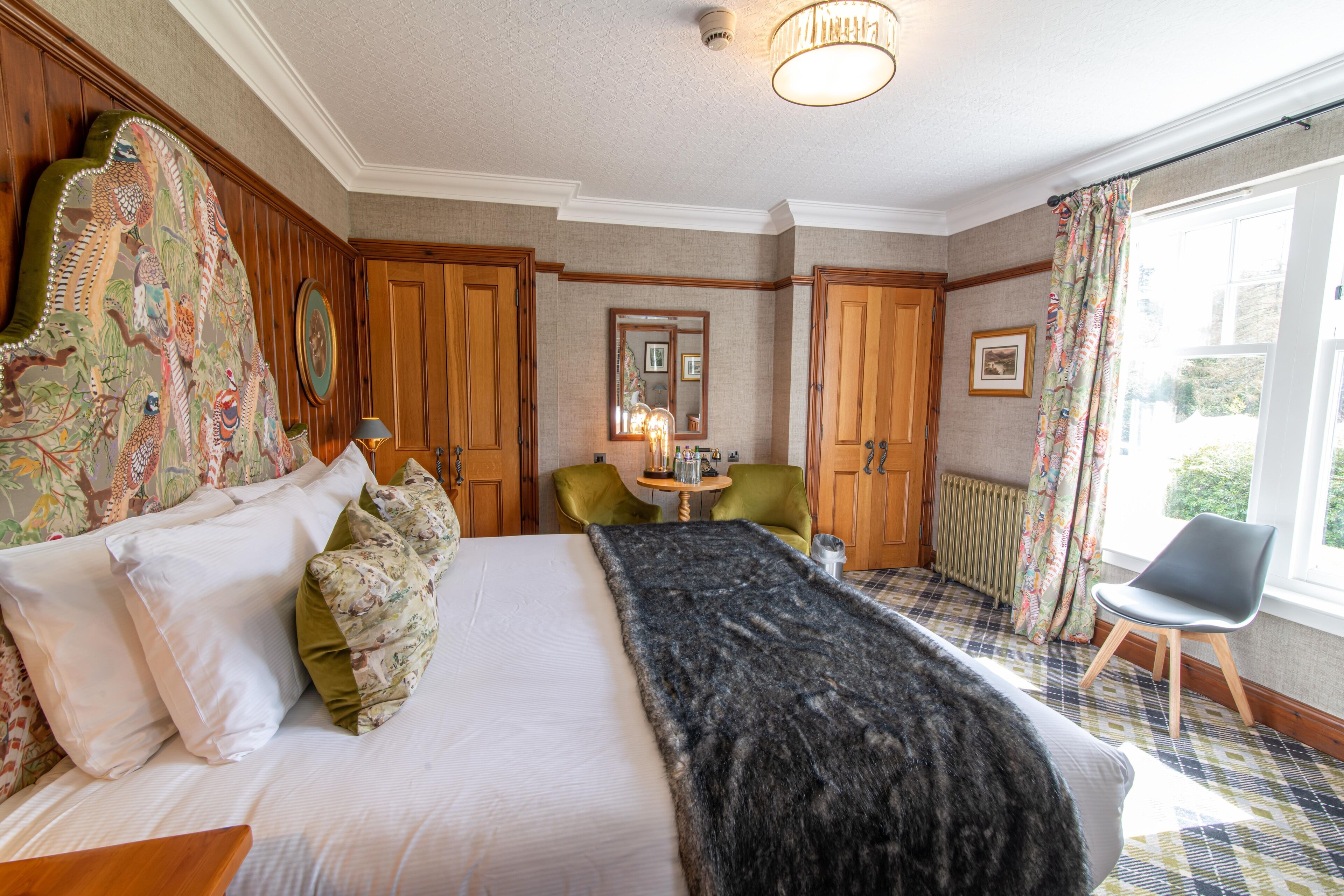 A hotel room with a large bed, a chair, a table with a lamp, and a window with curtains.