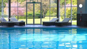 A swimming pool with lounge chairs and a view of a garden through large windows. - Dunkeld House Hotel (Dunkeld)