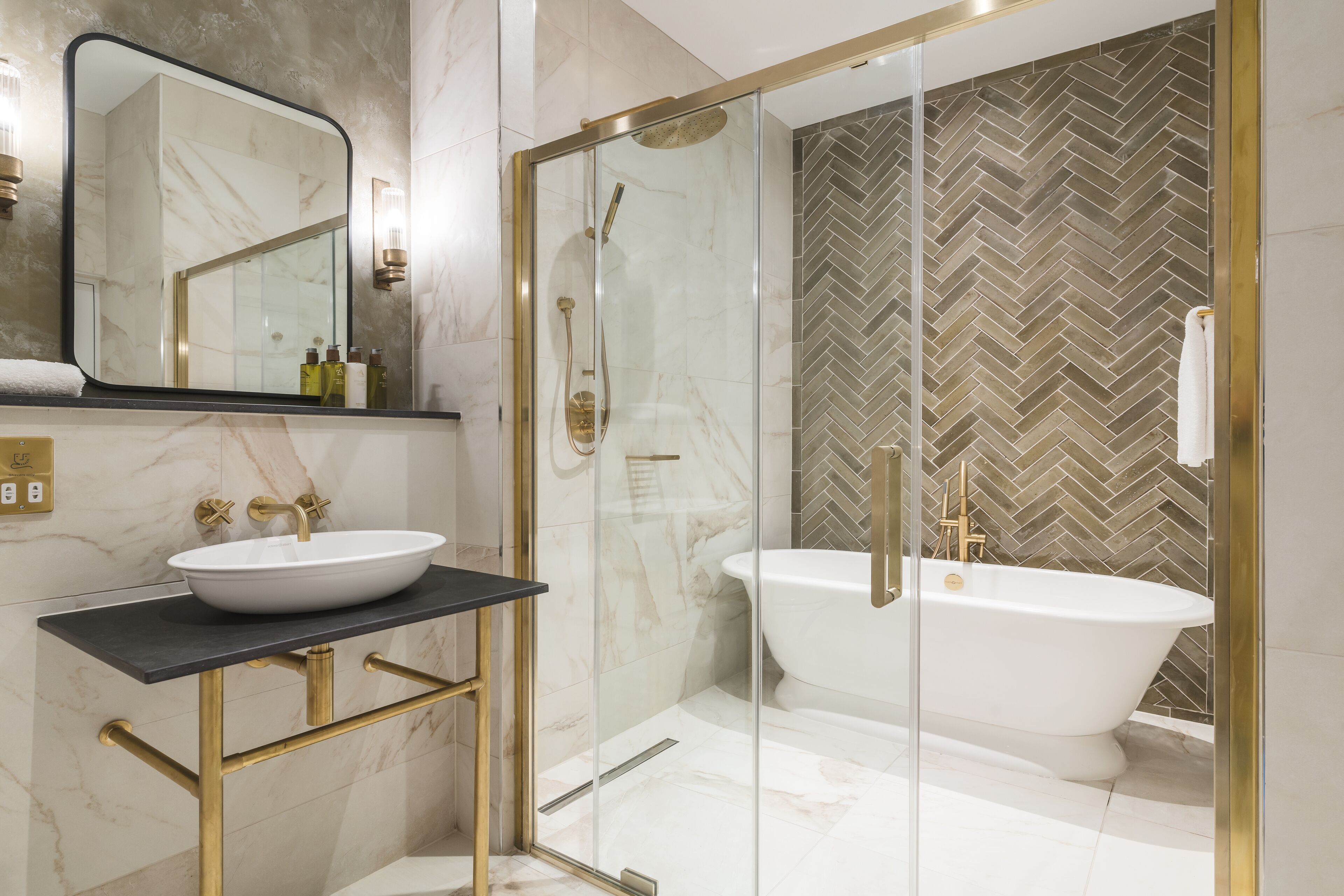 A modern bathroom with a glass-enclosed shower, a freestanding bathtub, and a marble vanity with a gold faucet.