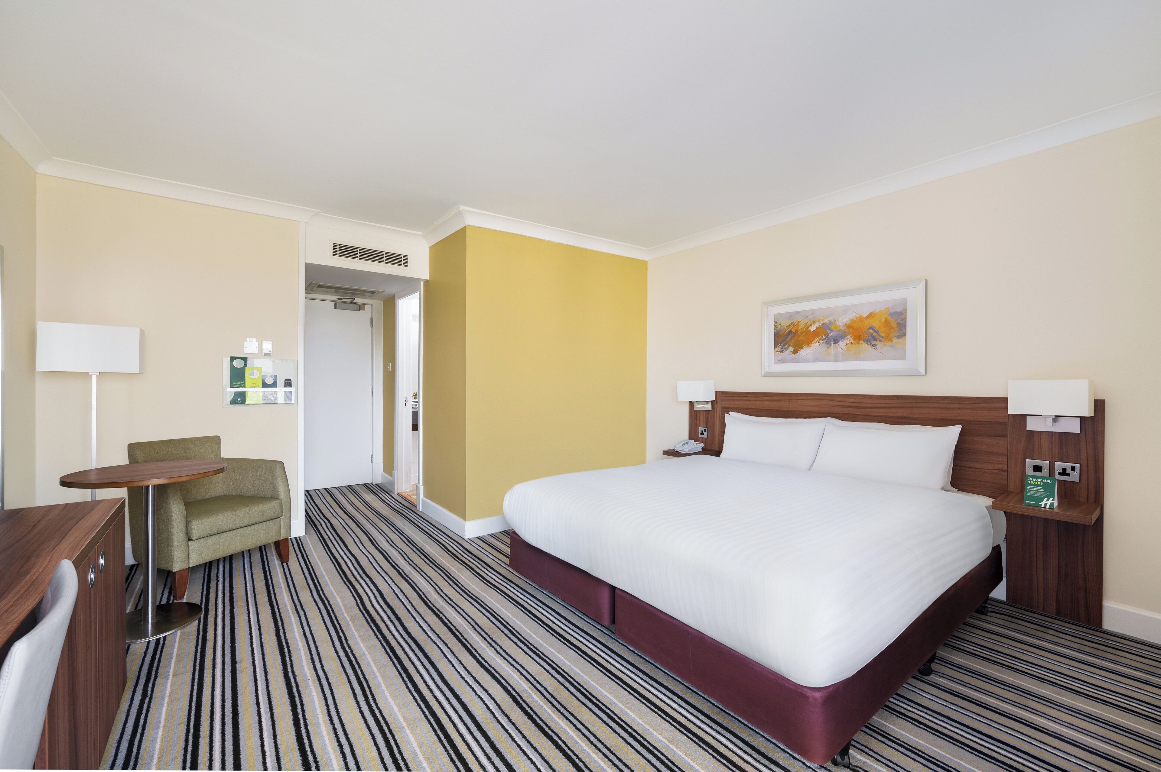 Quarto de hotel com uma cama grande, uma escrivaninha, uma cadeira e um quadro na parede.