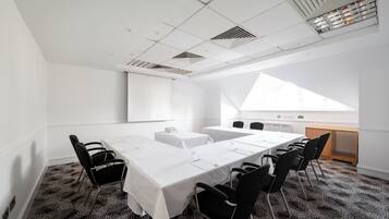 Un salón de conferencias con una larga mesa, sillas negras, una pantalla de proyector y un amplio ventanal.