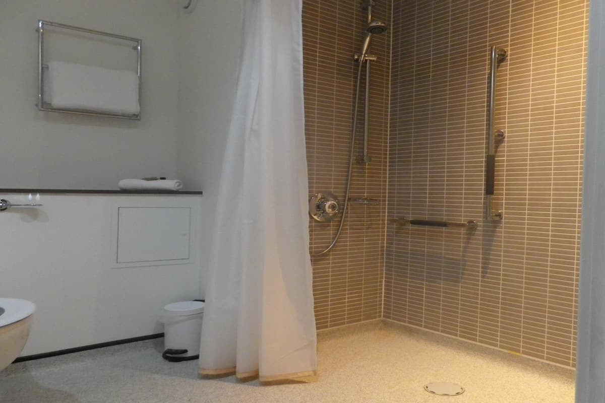 A small, tiled bathroom with a shower, toilet, and a towel rack.