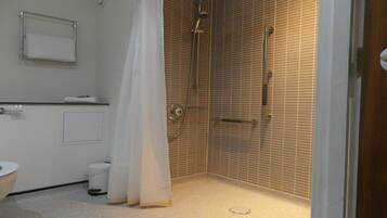 A small, tiled bathroom with a shower, toilet, and a towel rack.