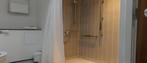 A small, tiled bathroom with a shower, toilet, and a towel rack.