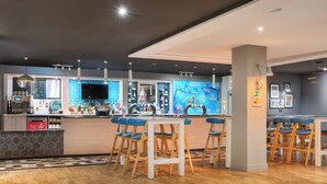 A modern bar area with wooden stools, a bar counter, and a blue-tiled wall with artwork. - Holiday Inn Glasgow East Kilbride by IHG (Glasgow)