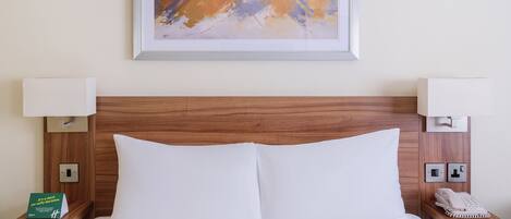 Una cama bien hecha con sábanas blancas, un cabecero de madera y dos mesitas de noche con lámparas y un teléfono.