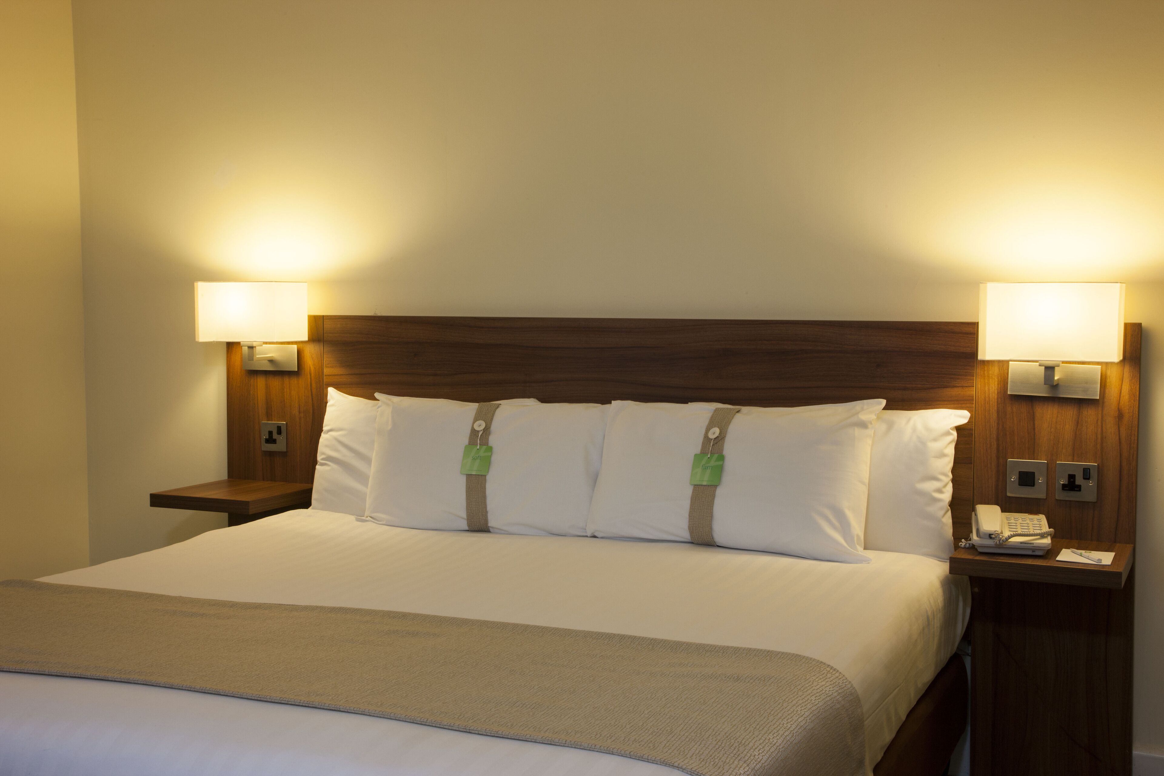 A hotel room with a large bed, two bedside tables with lamps, and a wooden headboard.