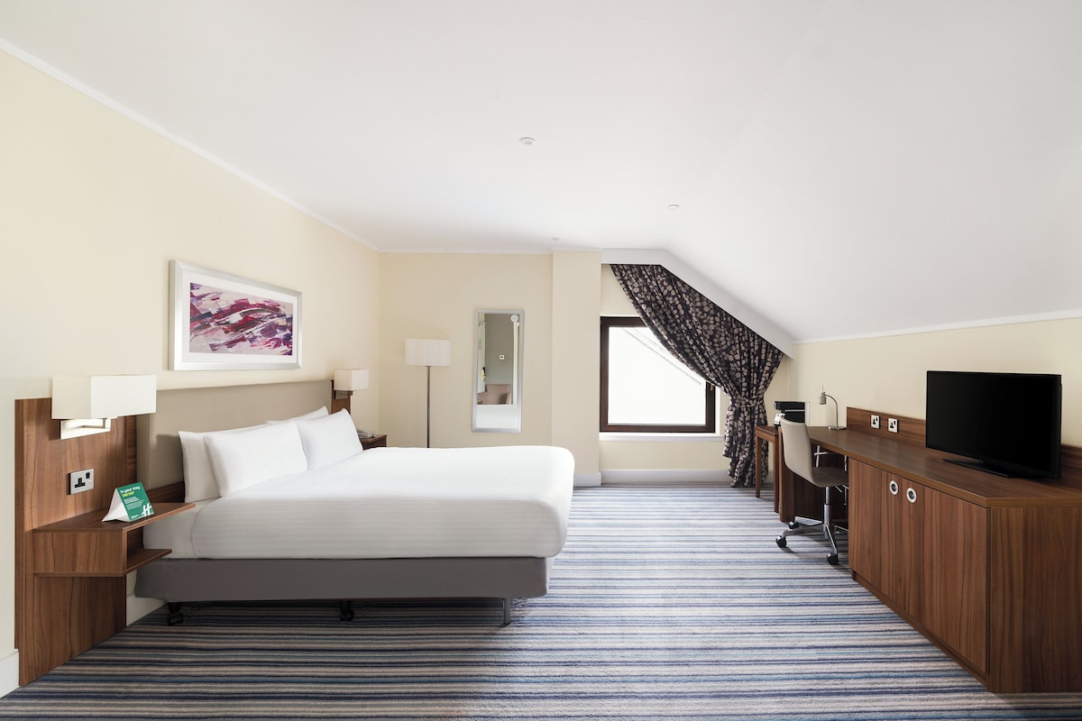 A hotel room with a bed, a desk, a television, a lamp, and a window with curtains.