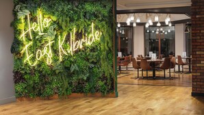 A modern interior with a neon sign reading "Hello, I love Kilbride" against a lush green wall, wooden flooring, and a dining area with chairs and tables. - Holiday Inn Glasgow East Kilbride by IHG (Glasgow)