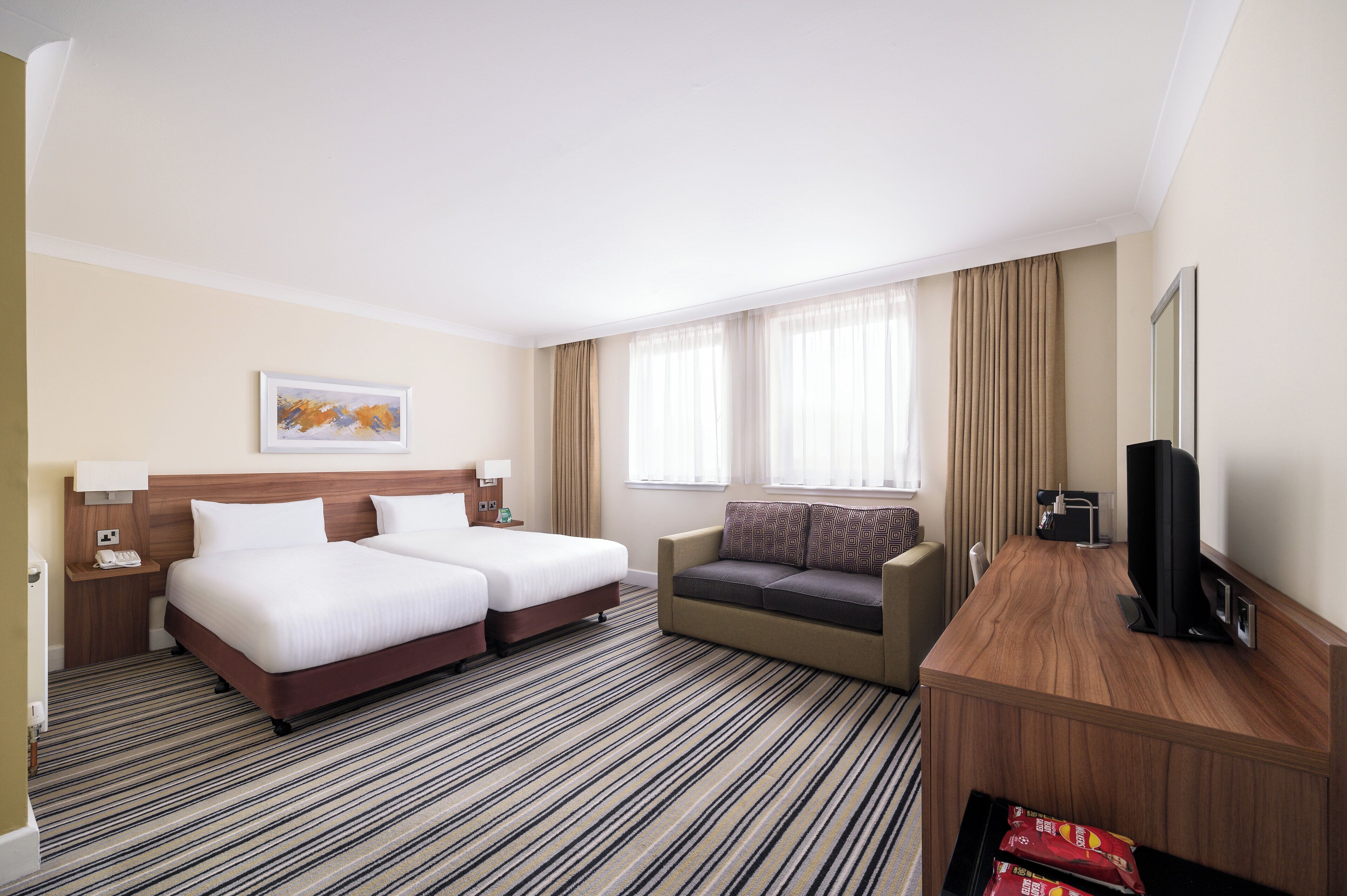Een hotelkamer met twee bedden, een bank, een televisie en een bureau.