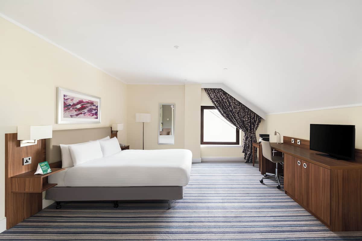 A hotel room with a bed, a desk, a television, a lamp, and a window with curtains.