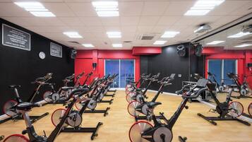 Ein Fitnessraum mit mehreren in Reihen angeordneten Ergometer, einer Uhr an der Wand und einem Farbkonzept in Rot und Schwarz.
