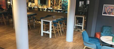 Una zona de bar con taburetes y una barra, un comedor con mesas y sillas, y una alfombra estampada en el suelo.