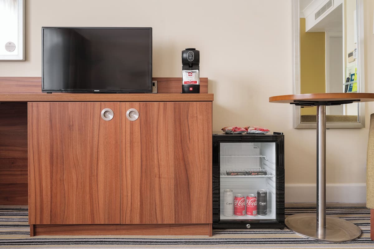 A wooden cabinet with a flat-screen TV, a coffee maker, and a mini-fridge with beverages.