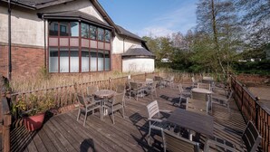 A building with a corner window, outdoor seating area with tables and chairs, and a wooden deck. - Holiday Inn Glasgow East Kilbride by IHG (Glasgow)