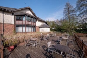 A building with a corner window, outdoor seating area with tables and chairs, and a wooden deck. - Holiday Inn Glasgow East Kilbride by IHG (Glasgow)