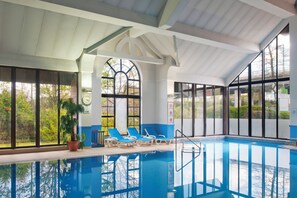 An indoor swimming pool with clear glass walls, blue lounge chairs, and a potted plant. - Holiday Inn Glasgow East Kilbride by IHG (Glasgow)