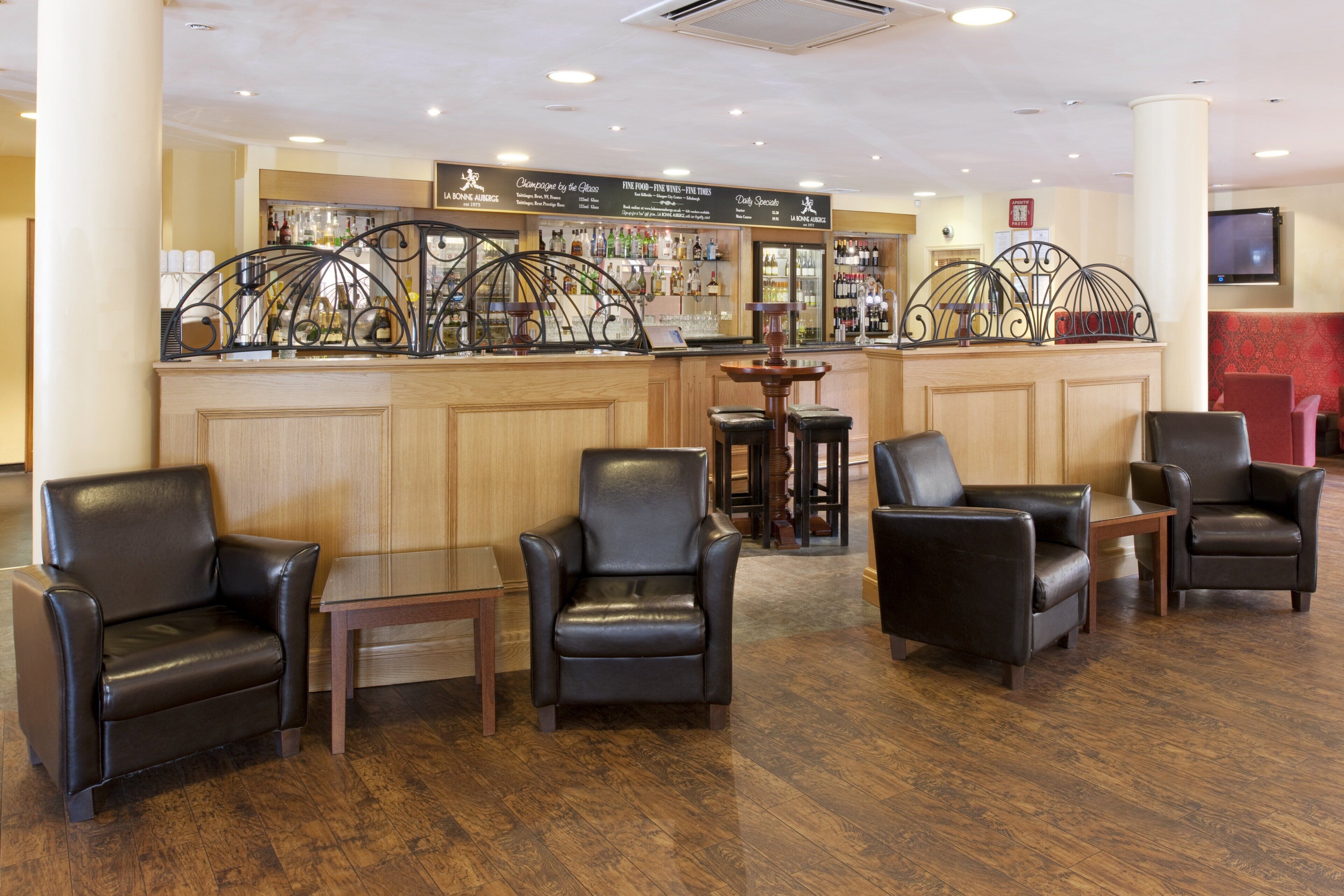 A bar area with a wooden counter, black leather chairs, and a menu board.
