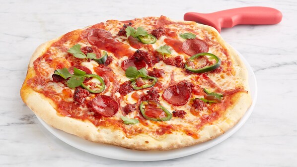 Pizza mit Peperoni, Jalapeños und Käse auf einem weißen Teller.