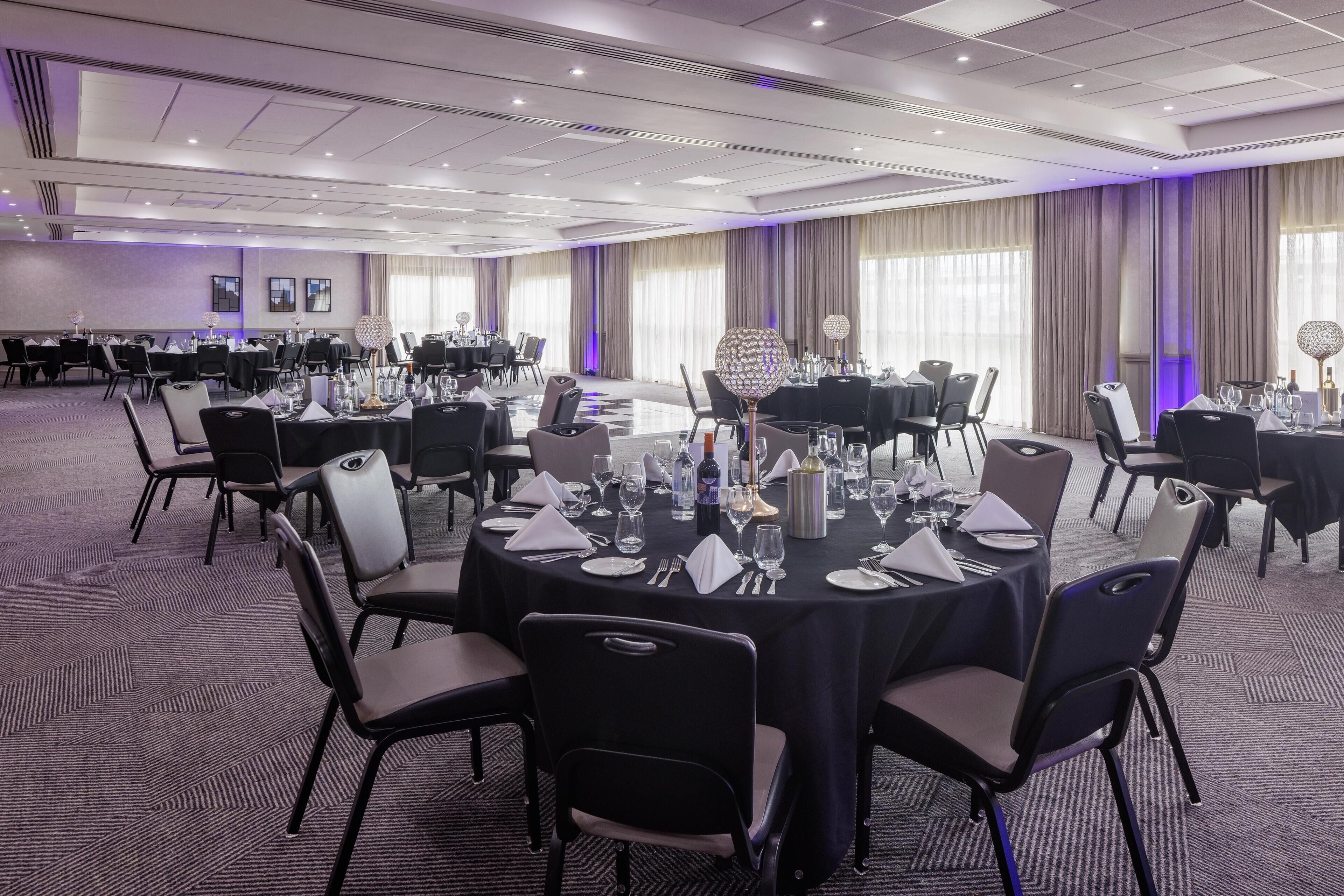 A conference room with round tables, chairs, and a carpeted floor.