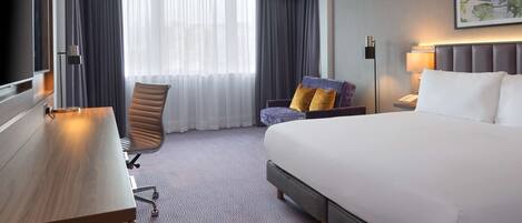 Una habitación de hotel con una cama grande, un escritorio, una silla y un televisor.