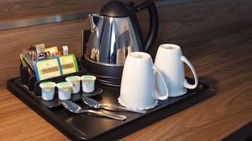 Una bandeja con una cafetera, dos tazas blancas, una cuchara, un cuchillo y varios alimentos envasados.