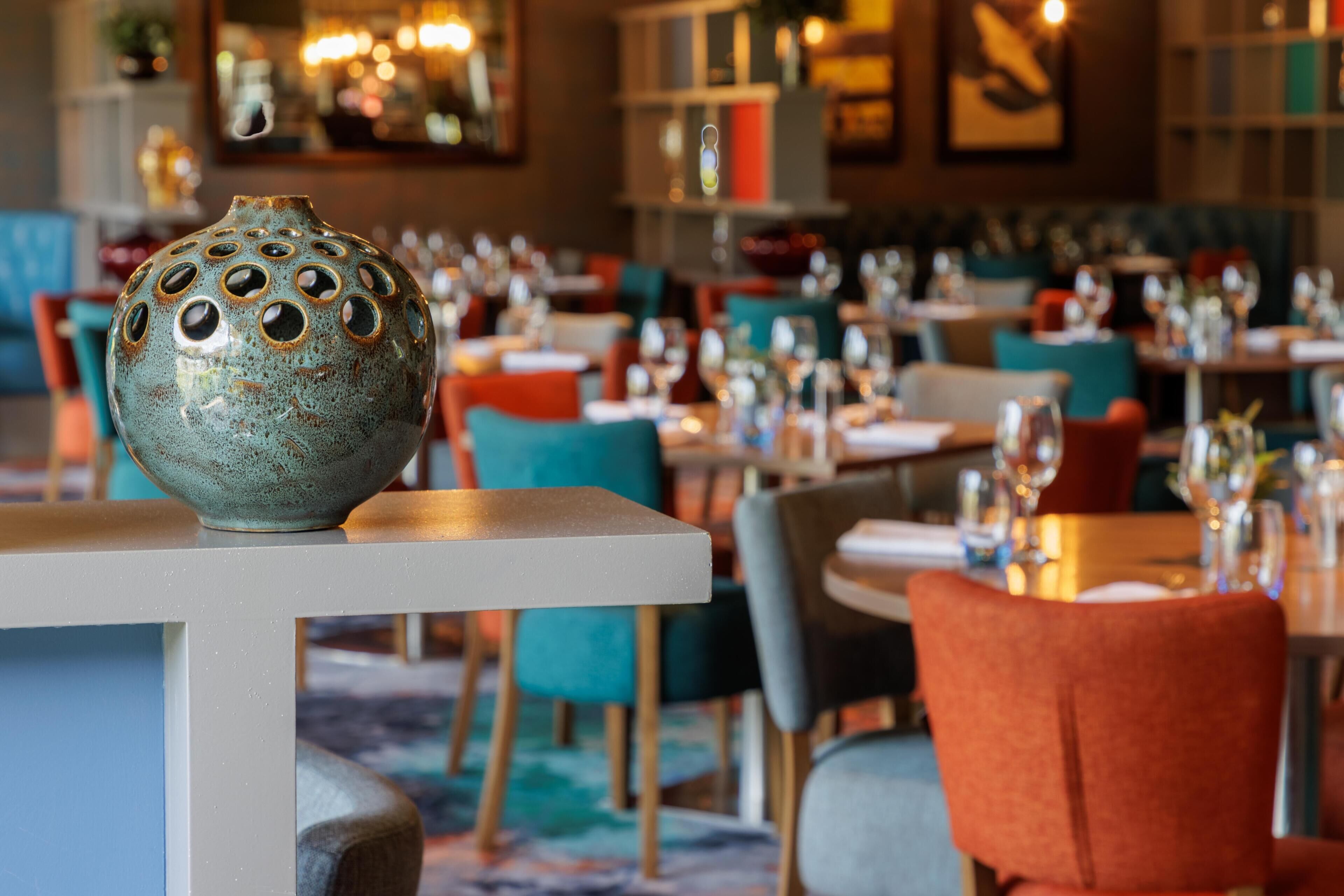 Comedor con mesas dispuestas para recibir a comensales, destacando un jarrón de cerámica decorativo sobre una de ellas.