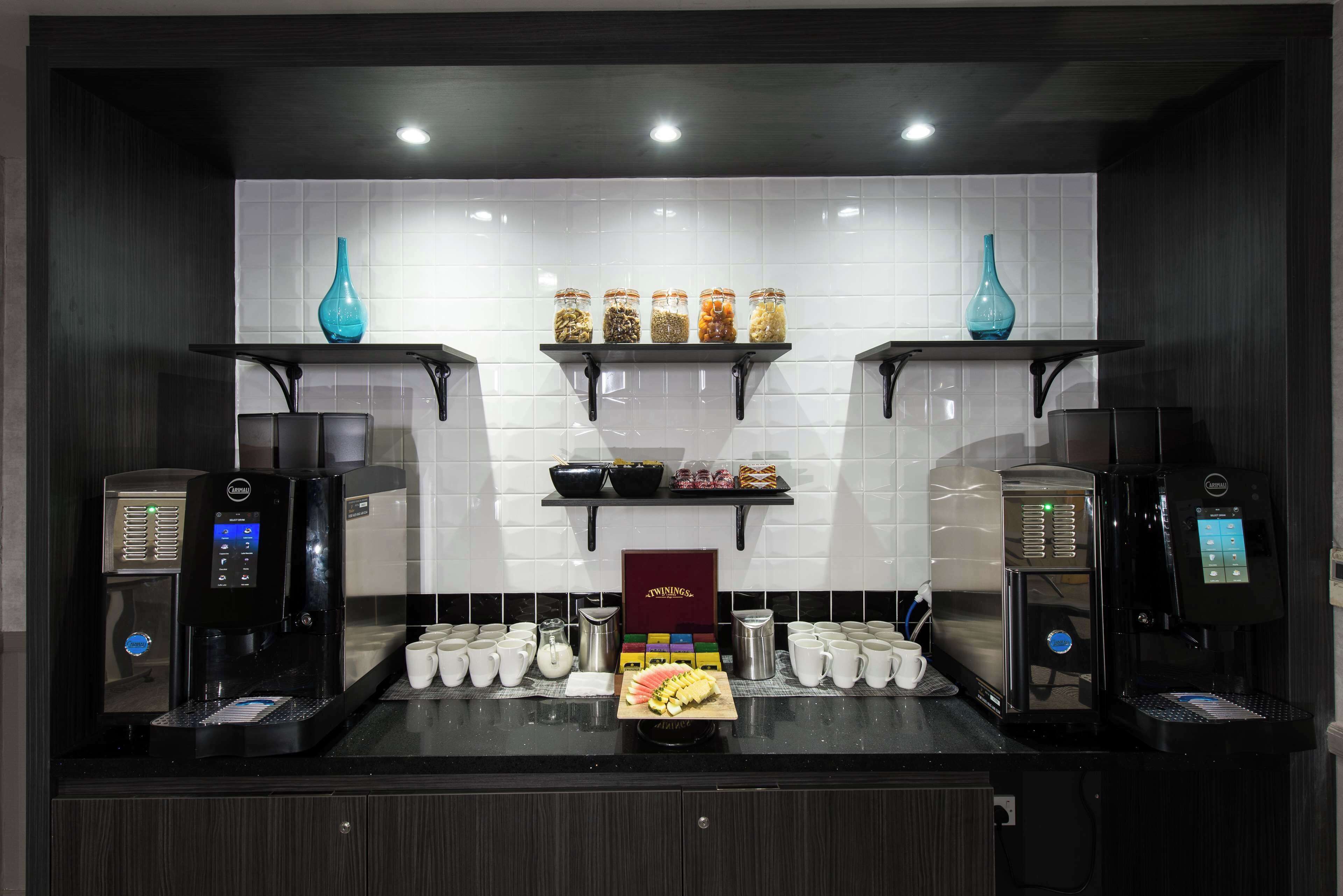 A coffee station with two espresso machines, a display of coffee pods, and a variety of jars on shelves.