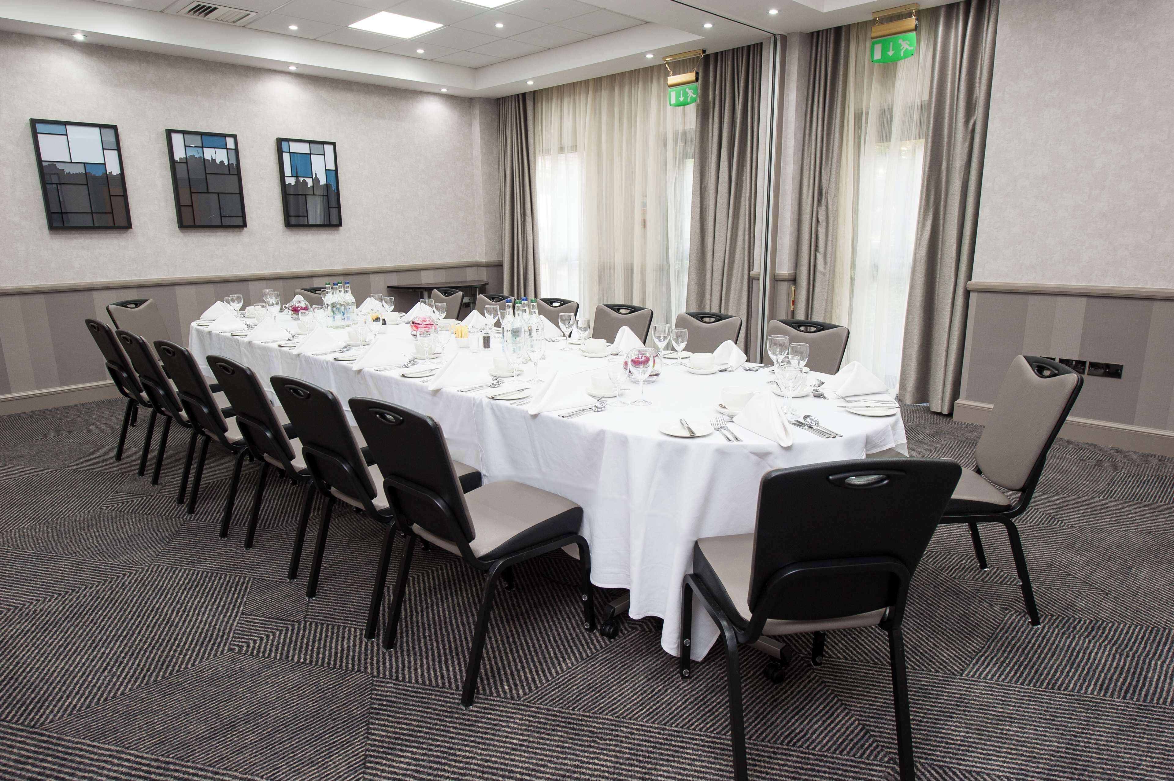 A conference room with a long table set for a meeting, equipped with chairs, a white tablecloth, and various dining utensils.