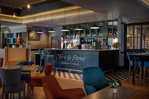 Zona de bar con un letrero que dice 'Olive & Stone Kitchen Cocktails' y una variedad de botellas y vasos en estantes.