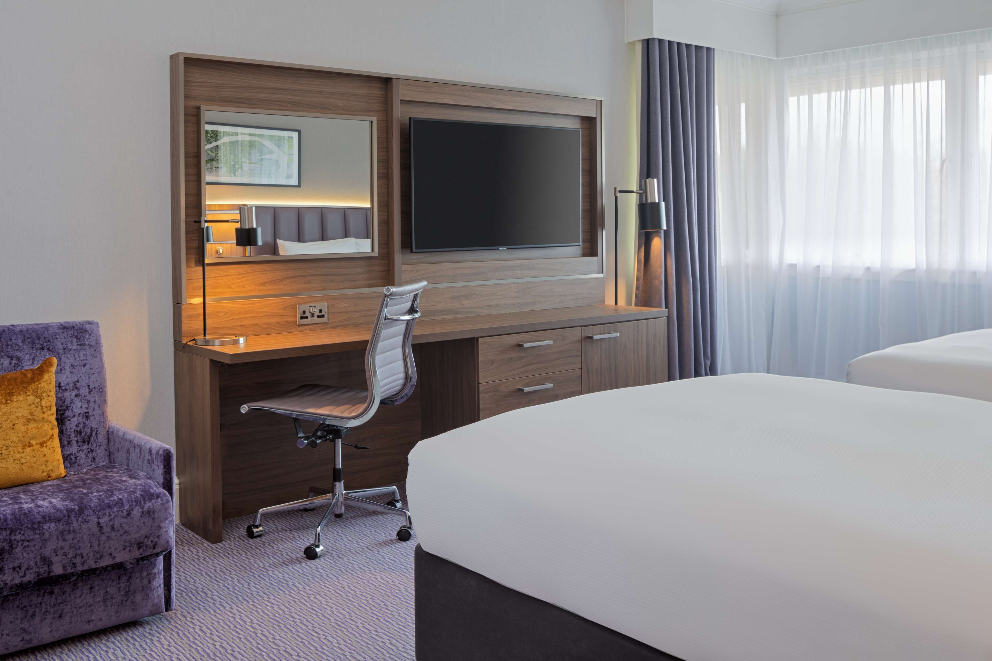 Une chambre d’hôtel avec un grand lit, un bureau avec une chaise, une télévision et une fenêtre avec des rideaux.