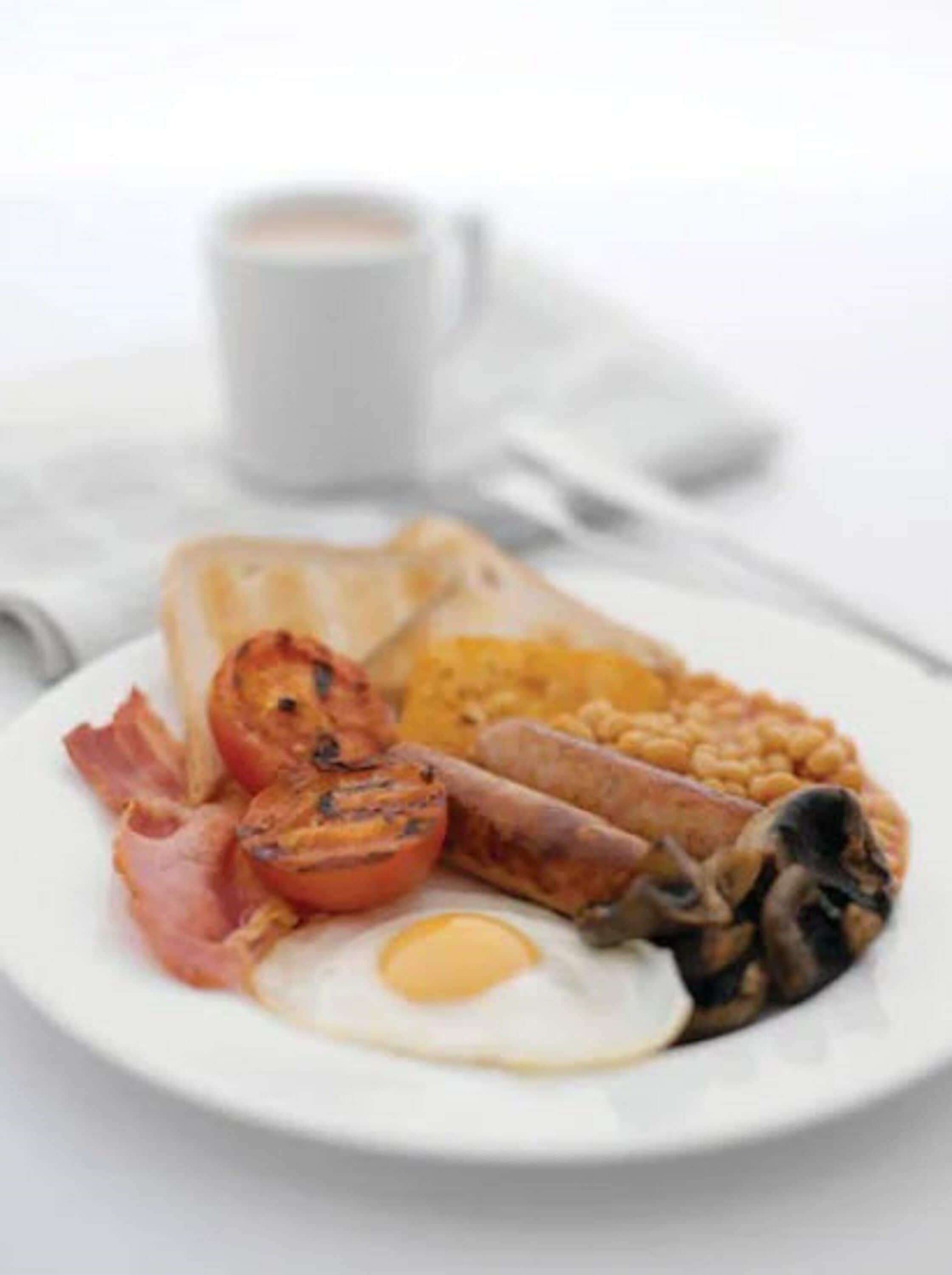 A plate of breakfast food including eggs, bacon, tomatoes, beans, and toast.