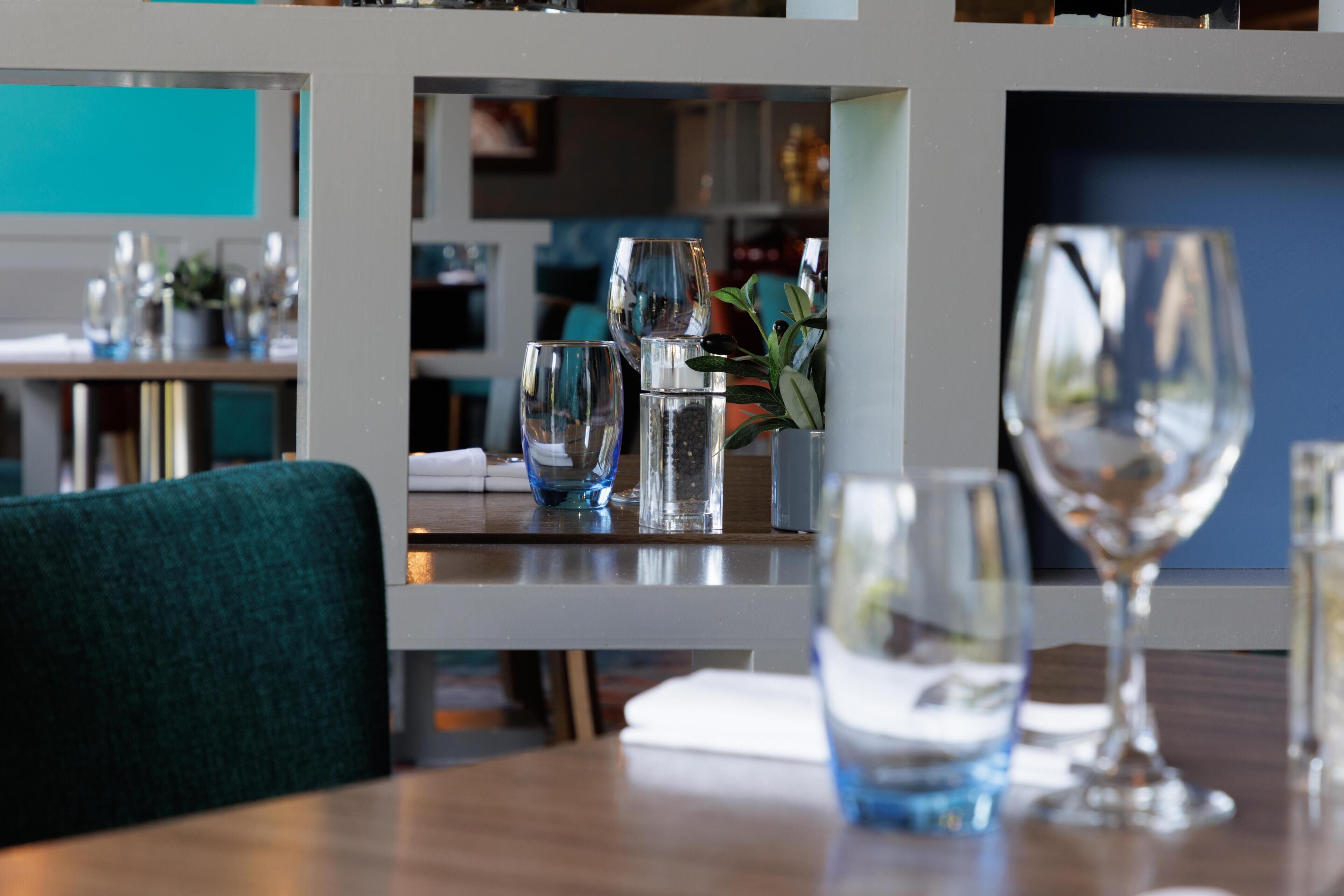 En restaurangmiljö med ett dukat bord, inklusive glas och en vas med en växt.
